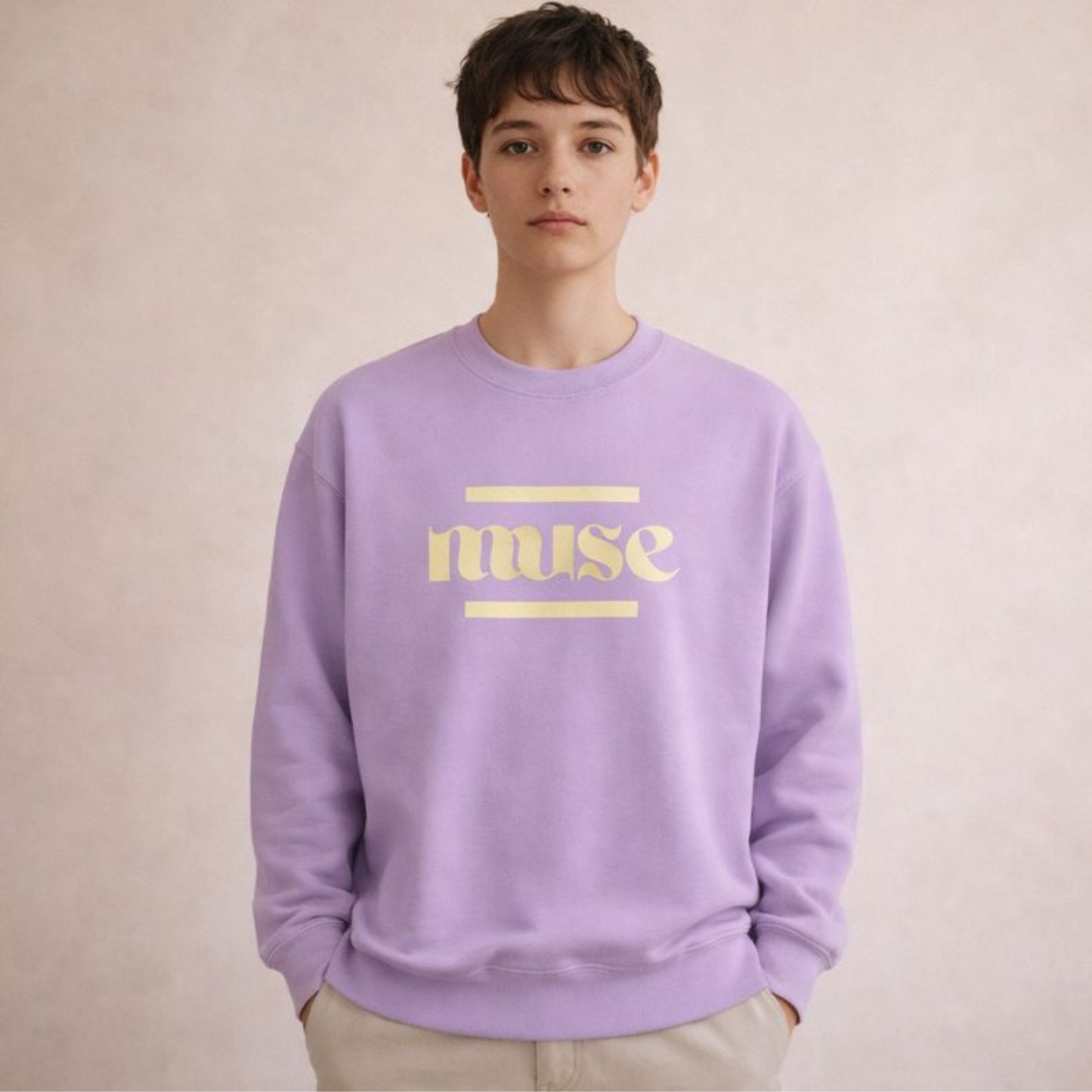 Lavender unisex crewneck sweatshirt featuring “muse” typography graphic, relaxed studio pose against a soft beige gradient backdrop.